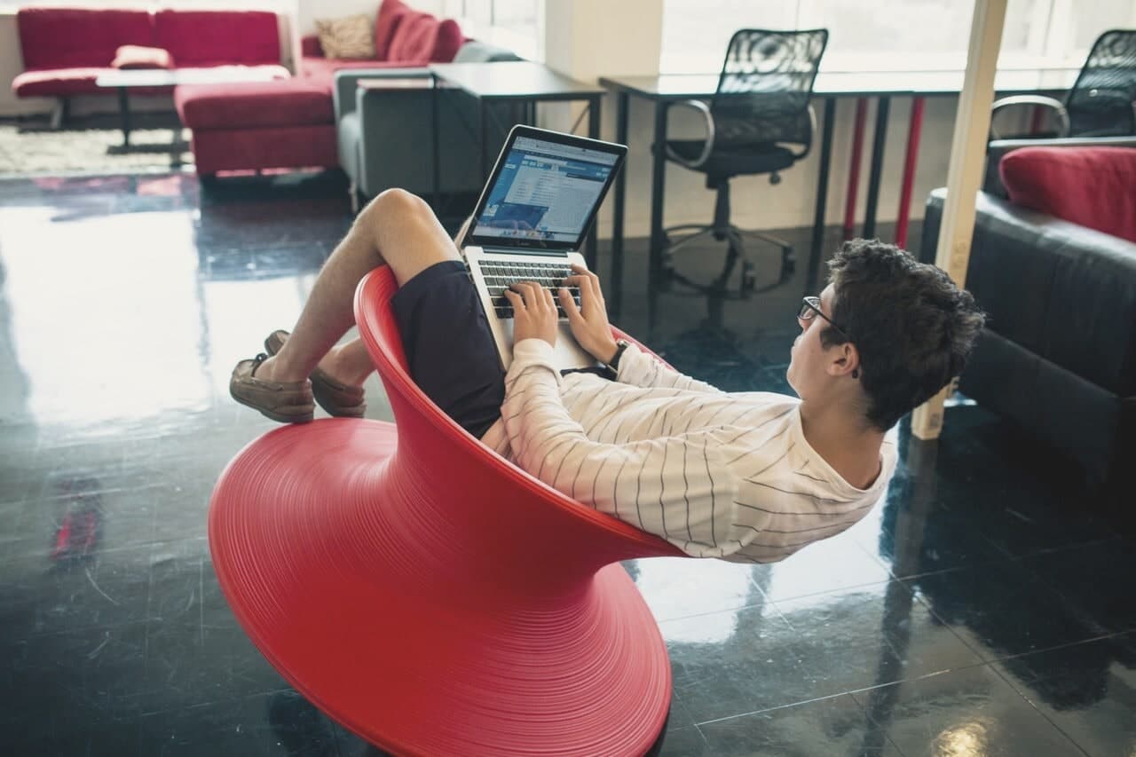 A member working on a laptop while reclining in a red spinner chair on the Geekdom floor.